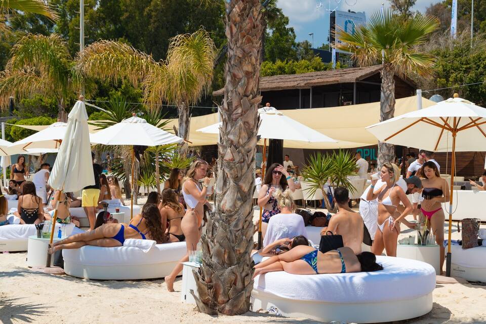Ein Hotel direkt am Strand mit Liegestühlen, Palmen und Sonnenschirmen.