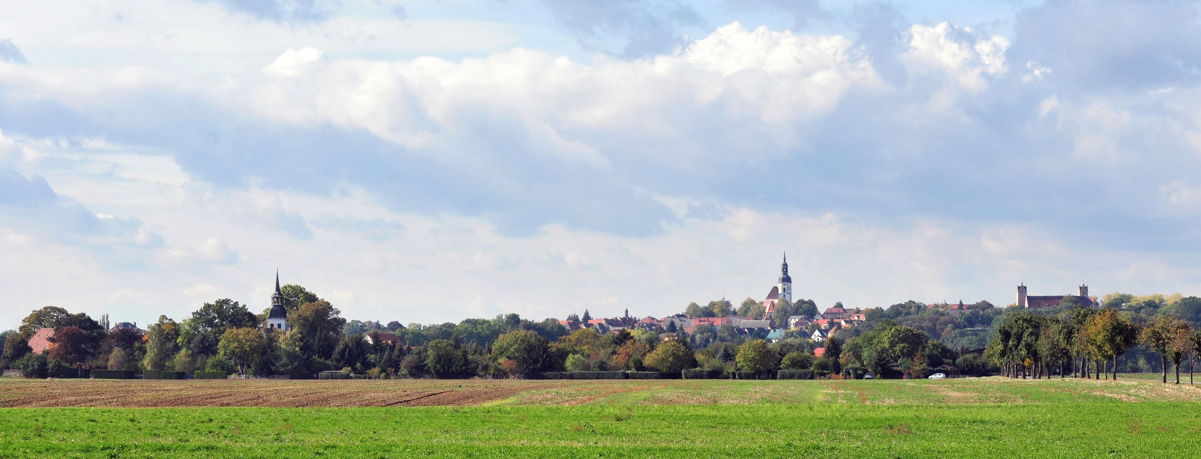 A rural landscape with fields, trees, and a distant town with a church tower.