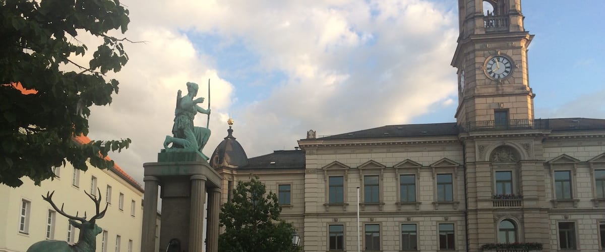 A square with a statue, a clock tower, and classical architecture.