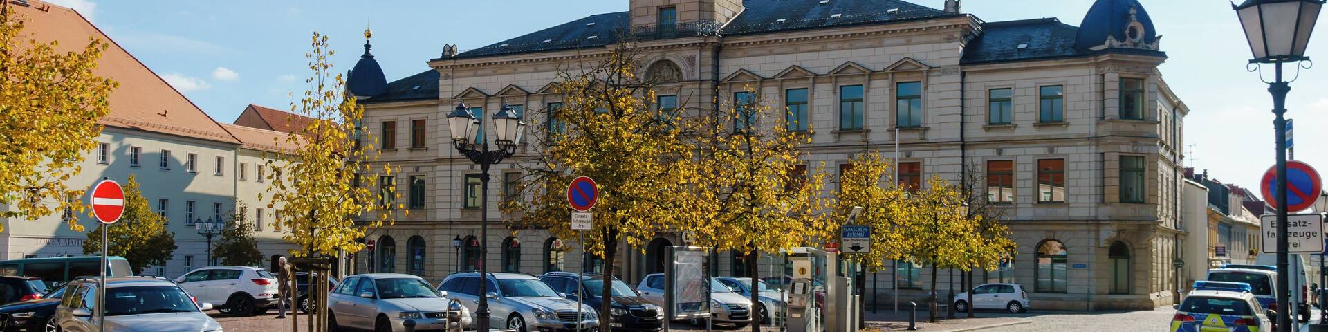 A historic building with a clock tower, parked cars, and autumn trees.