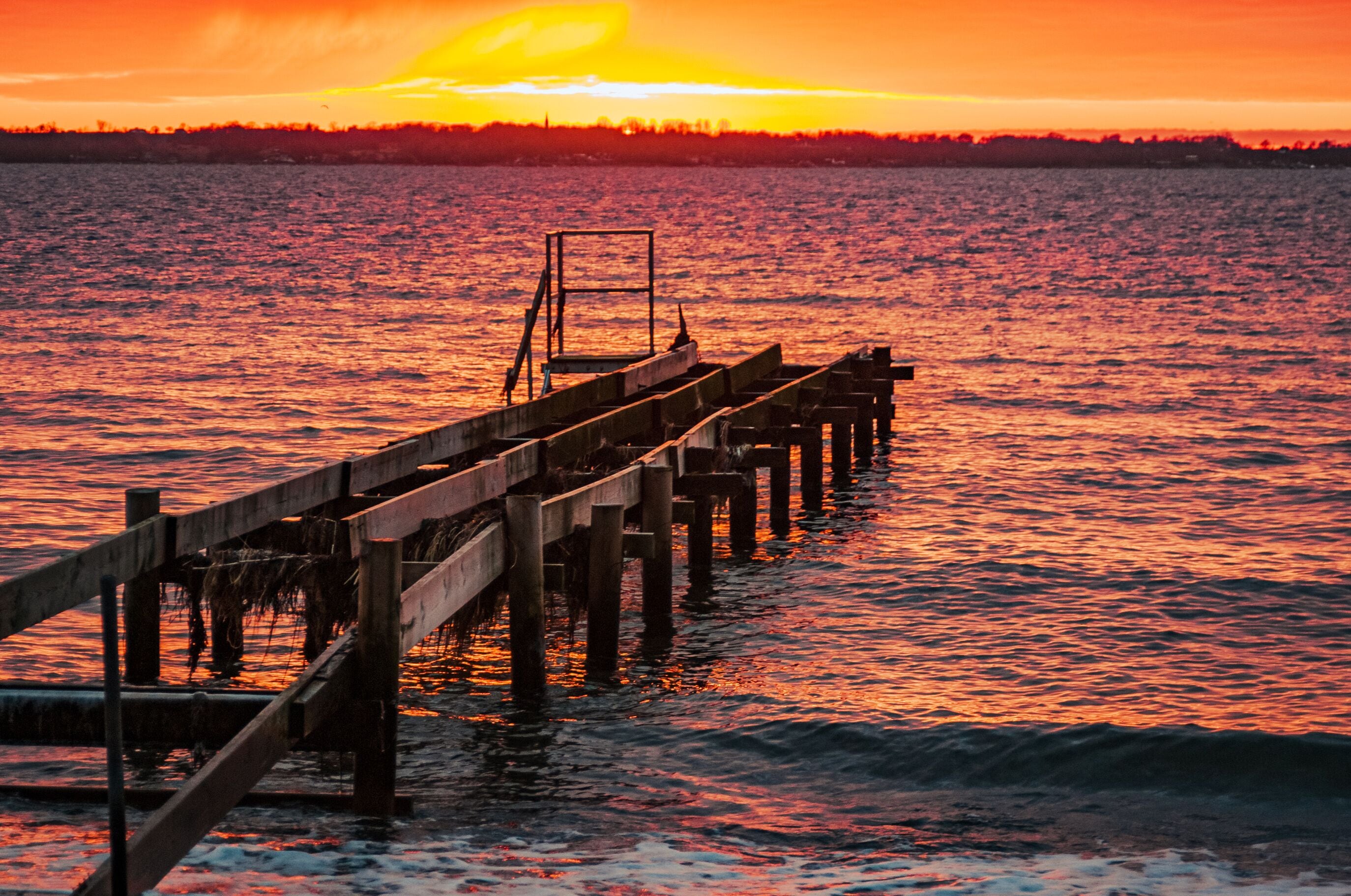A wooden pier extending into a body of water during sunset.