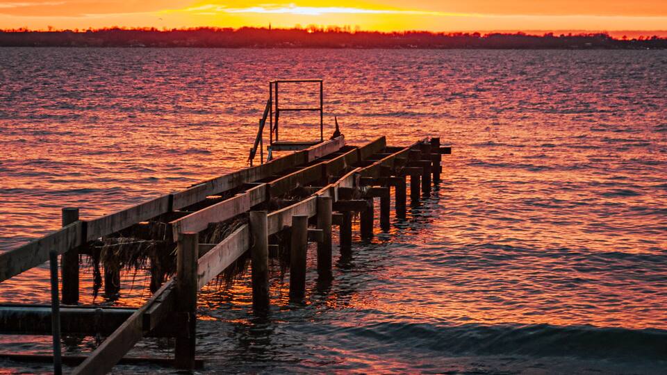 A wooden pier extending into a body of water during sunset.