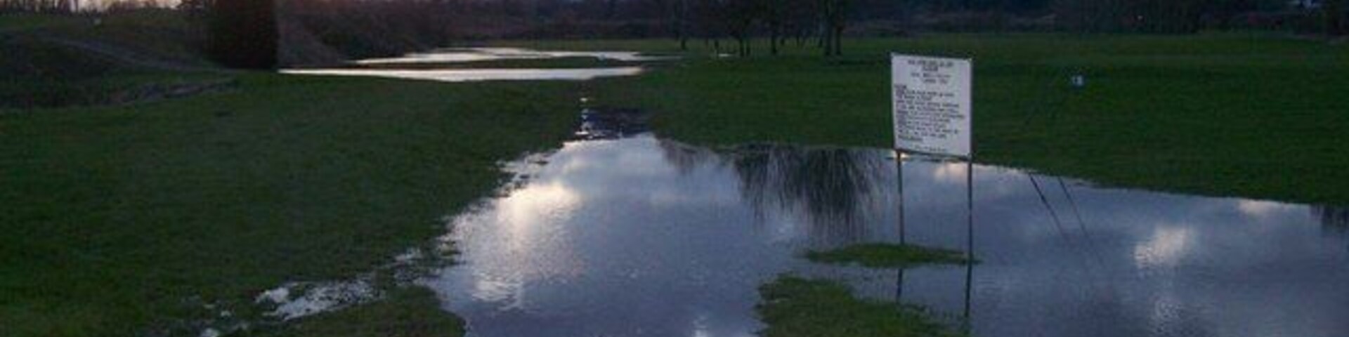 Un campo inundado con un cartel y un sendero que lo atraviesa.