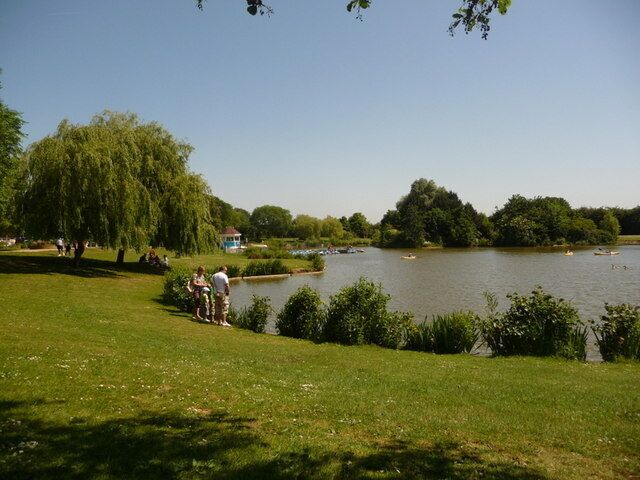 A park with a lake, trees, and people walking.