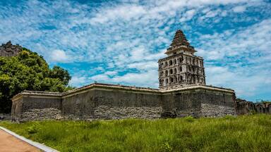 A historical stone building with a tower, surrounded by lush greenery and a clear blue sky.