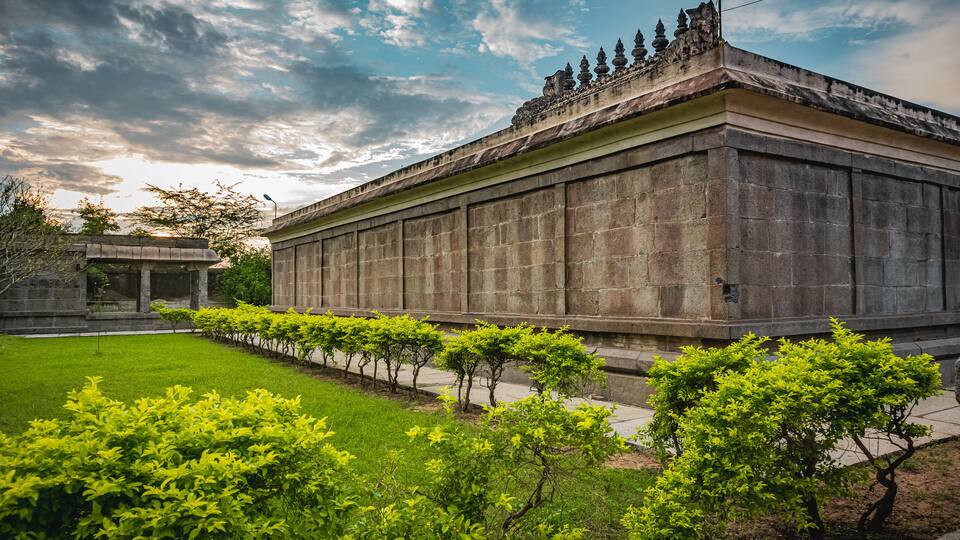 A large stone building with a flat roof and a row of small trees in front.