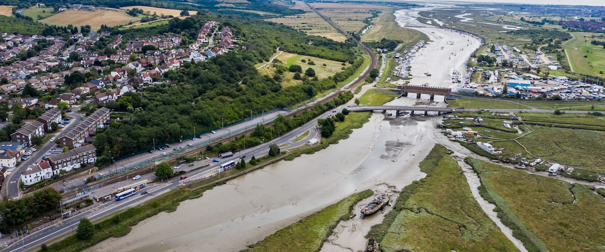 An aerial view of a river flowing through a town with a bridge, roads, and surrounding fields.