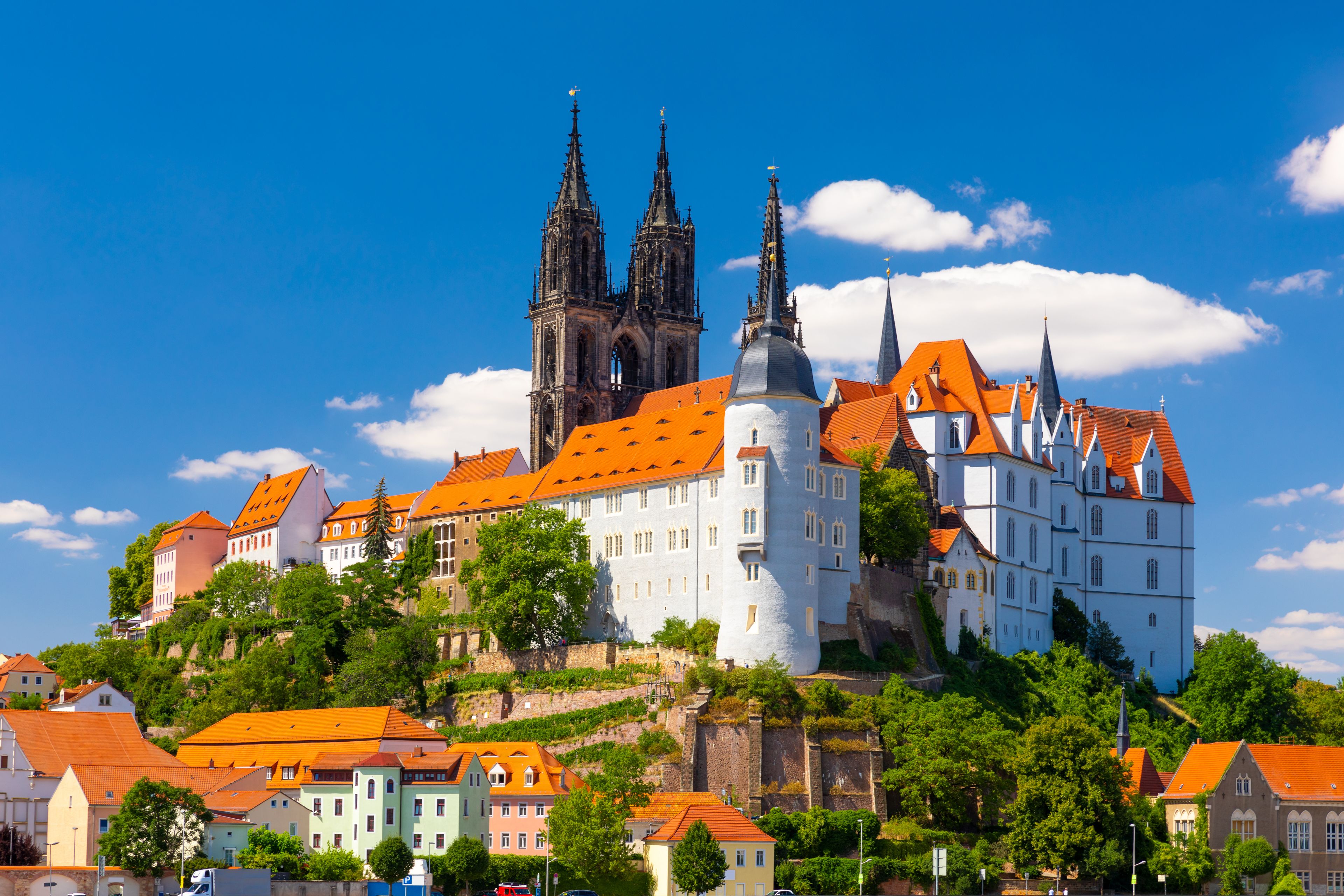 A historic castle with a prominent church, surrounded by colorful buildings and lush greenery.