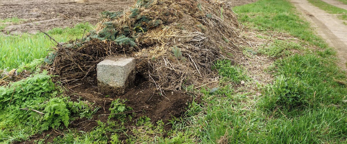A rural landscape with a pile of hay and a stone marker on a dirt path.