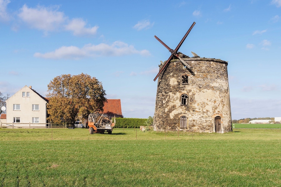 Un moulin à vent, une maison et un camion, le tout situé dans un cadre rural.