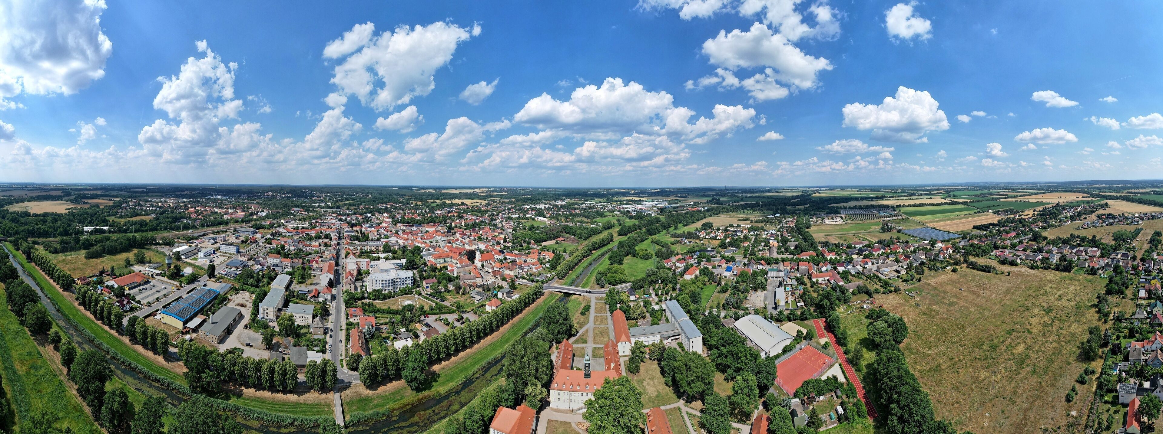 An aerial view of a town with a river, green fields, and a bridge.