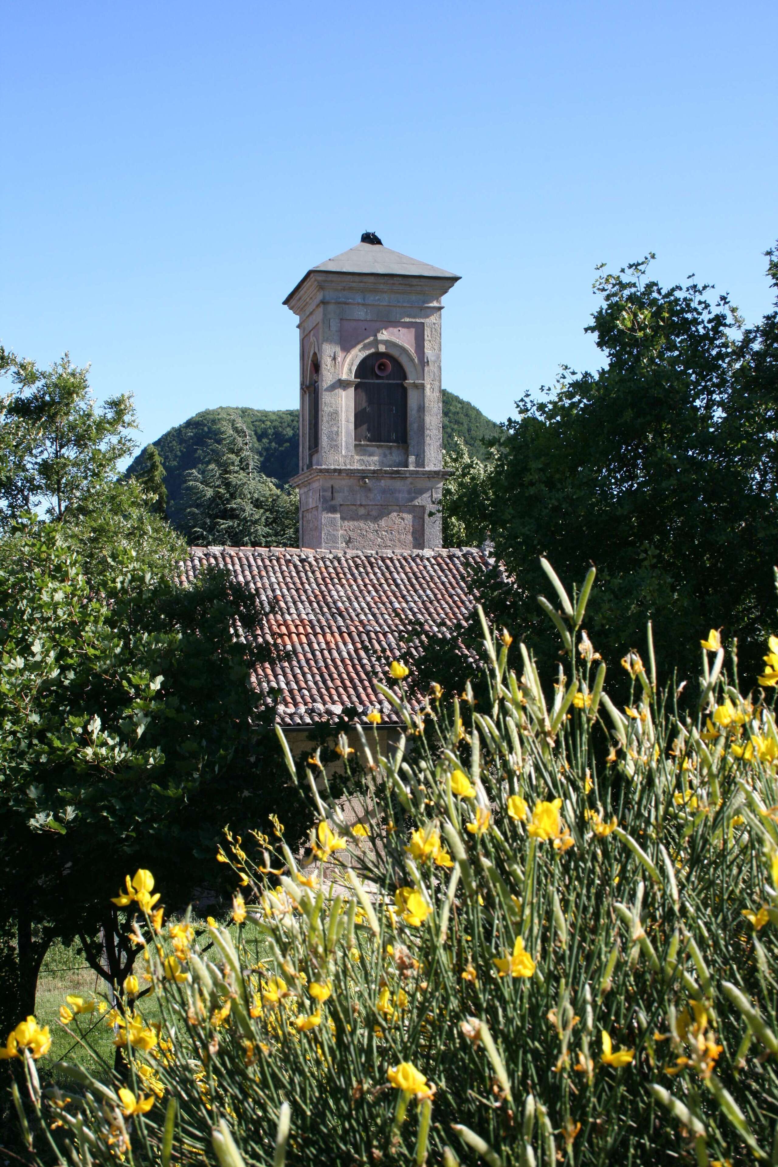A tower with a bell, surrounded by trees and yellow flowers.