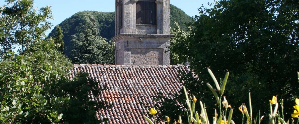 A tower with a bell, surrounded by trees and yellow flowers.