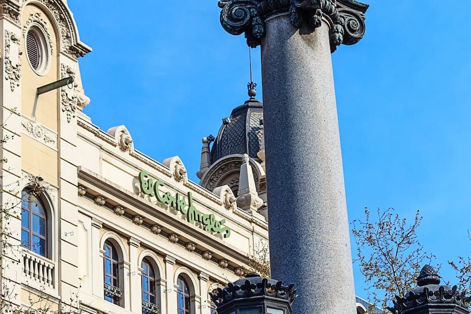 A historic building with ornate architecture, a tall column with decorative lanterns, and a clear blue sky.