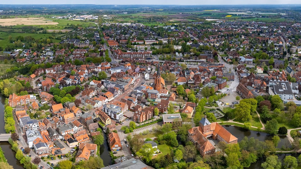 Luftaufnahme einer Stadt mit einem Fluss, grünen Feldern und einer Mischung aus Wohn- und Geschäftsgebäuden.