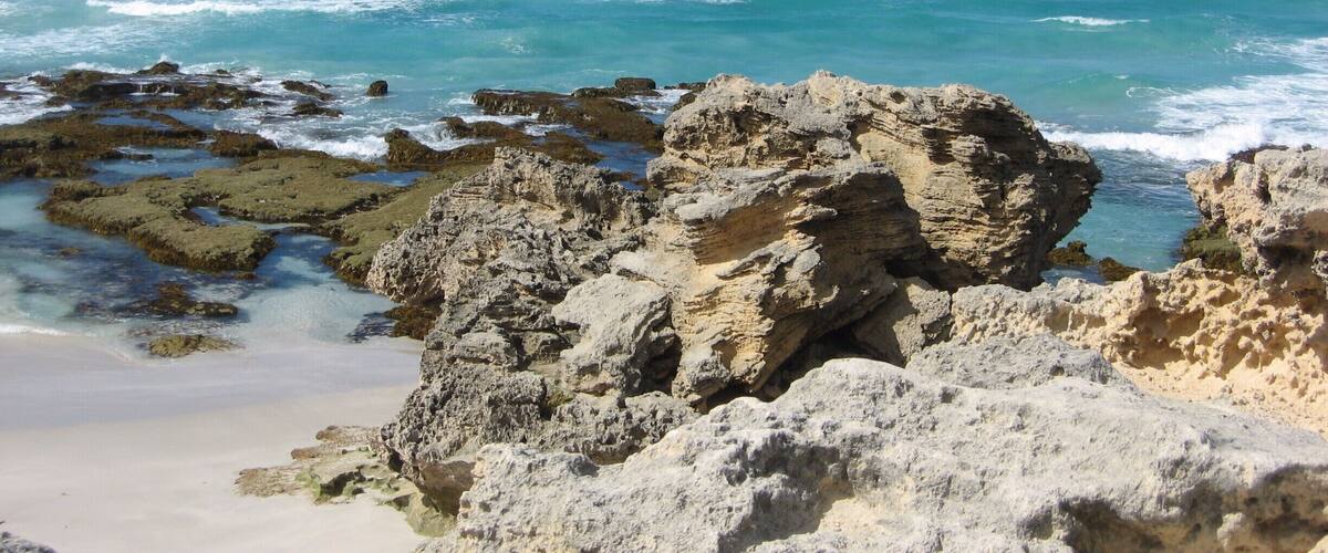 A rocky coastline with clear blue waters and waves crashing against the rocks.