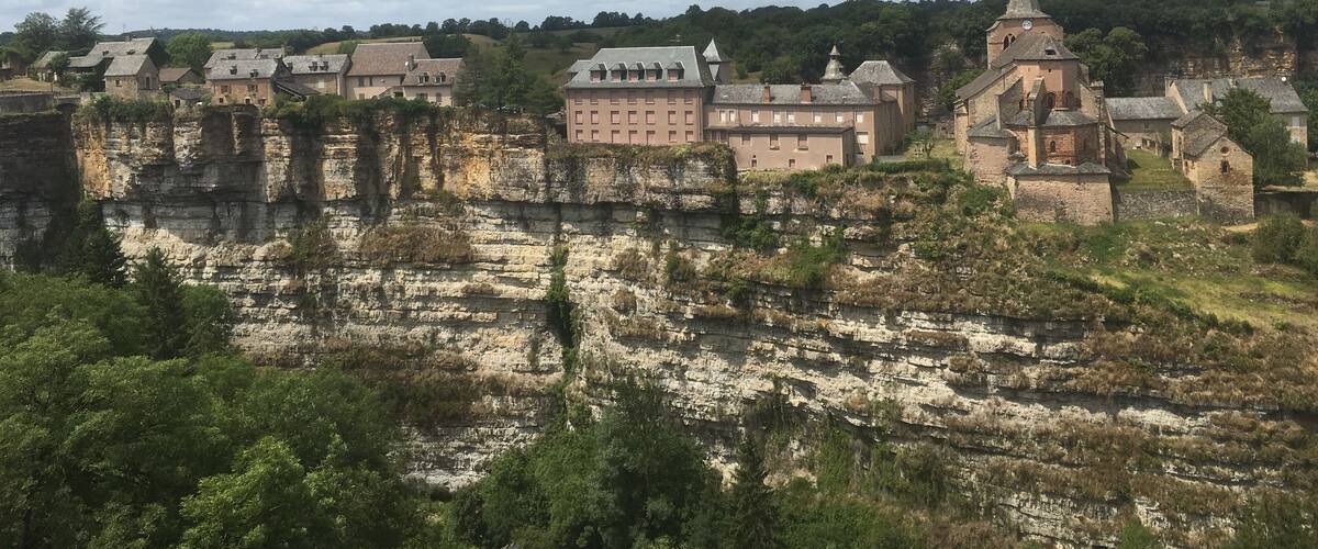 A historic town with medieval architecture, including a church with a tall spire, set against a backdrop of cliffs and a river.