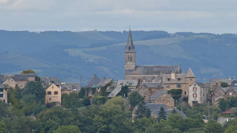 A historic town with a prominent church featuring a tall spire, surrounded by rolling hills and traditional stone buildings.