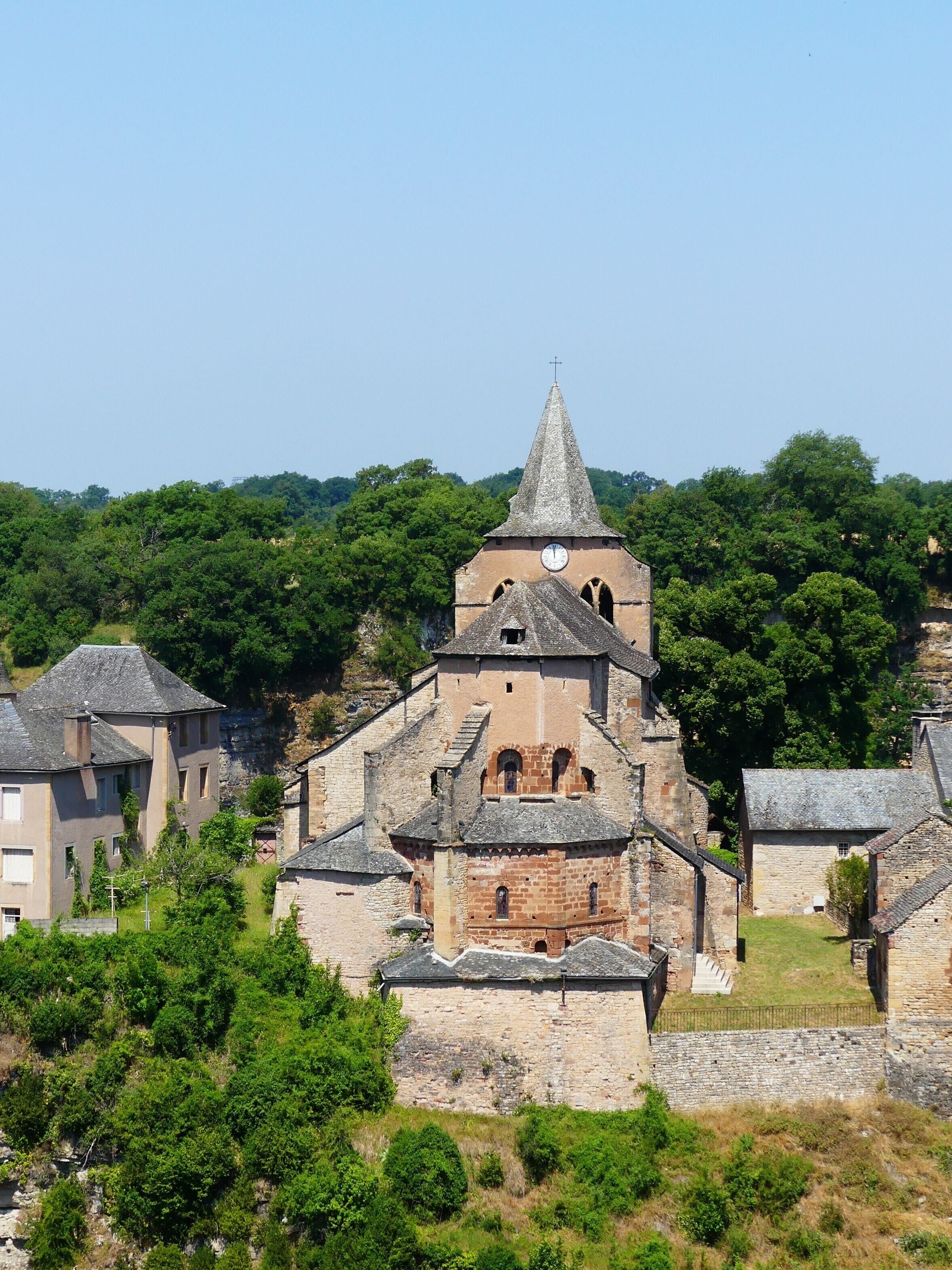 A historic church with a tall spire and clock tower, surrounded by lush greenery and traditional stone buildings.