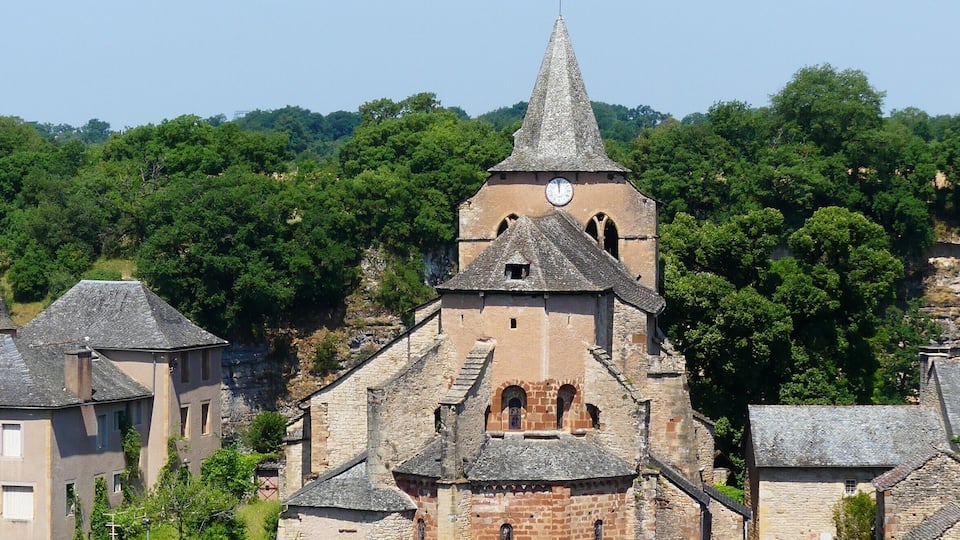 A historic church with a tall spire and clock tower, surrounded by lush greenery and traditional stone buildings.