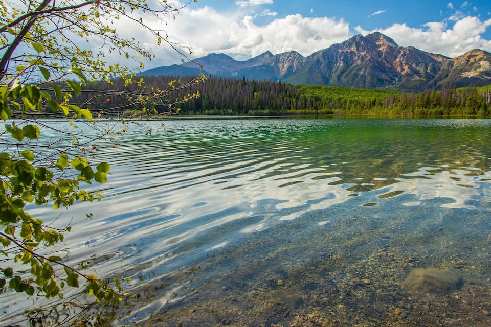 Un lac aux eaux limpides où l’on peut voir des galets, avec une chaîne de montagnes en arrière-plan.