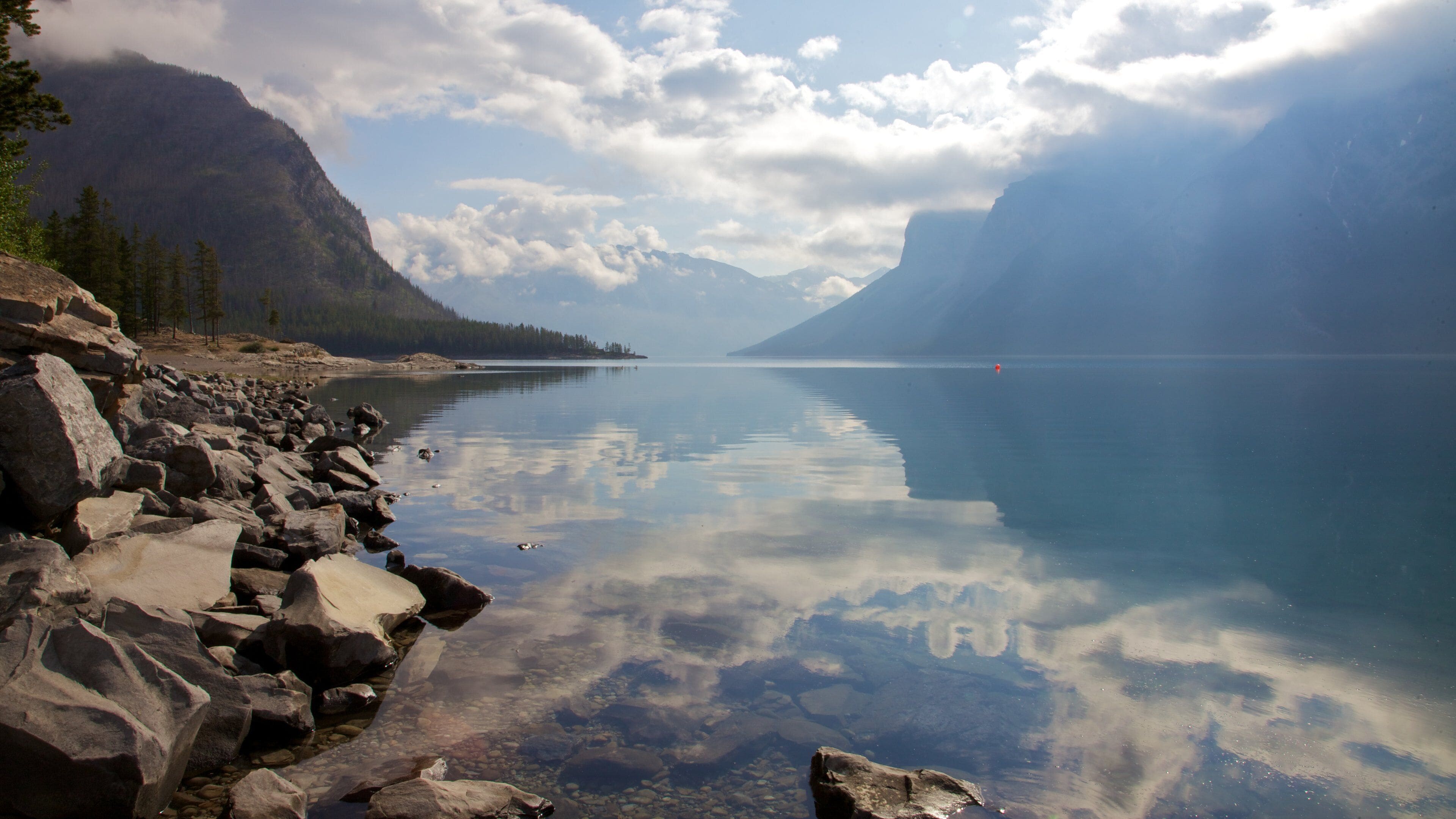 Ein ruhiger See mit klaren Spiegelungen, umgeben von Bergen und felsigen Ufern.