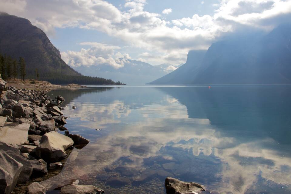 Ein ruhiger See mit klaren Spiegelungen, umgeben von Bergen und felsigen Ufern.