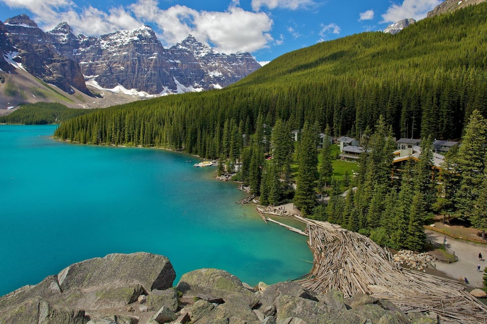 Un lago turchese circondato da fitte foreste e montagne con cime innevate.