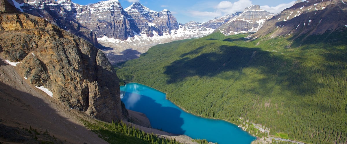 A mountain landscape with a turquoise lake surrounded by forest and snow-capped peaks.