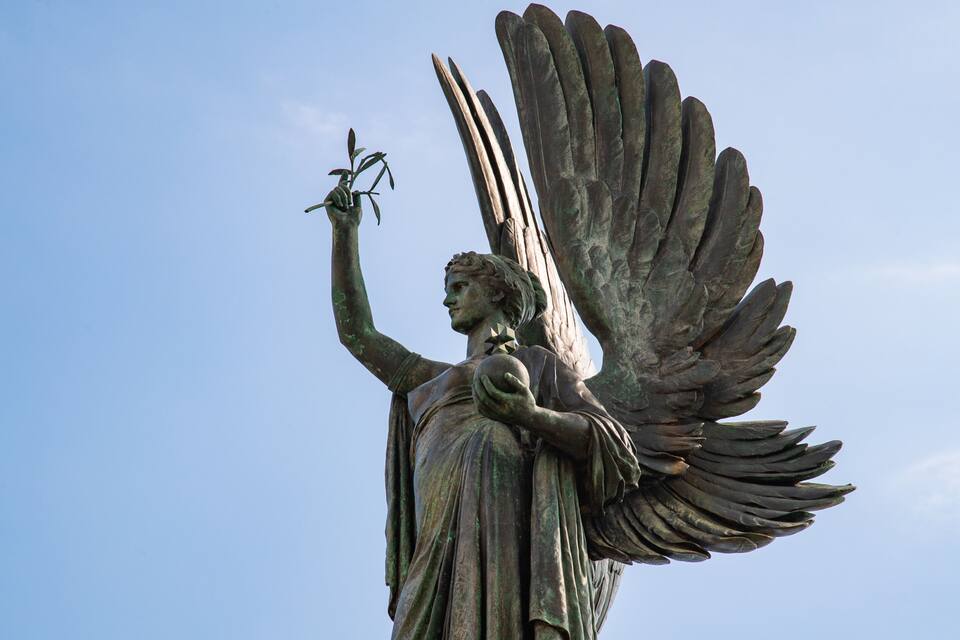 Eine Statue eines Engels mit ausgebreiteten Schwingen und einer Pflanze in der Hand.
