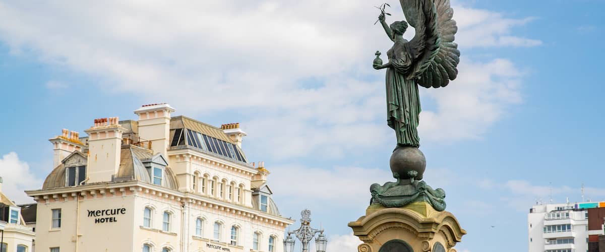 A statue of an angel with wings, a building labeled 'Mercure Hotel', and a clear sky with clouds.