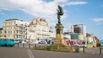 Et bybillede med en markant statue af en engel, omgivet af historiske bygninger og moderne skyskrabere.