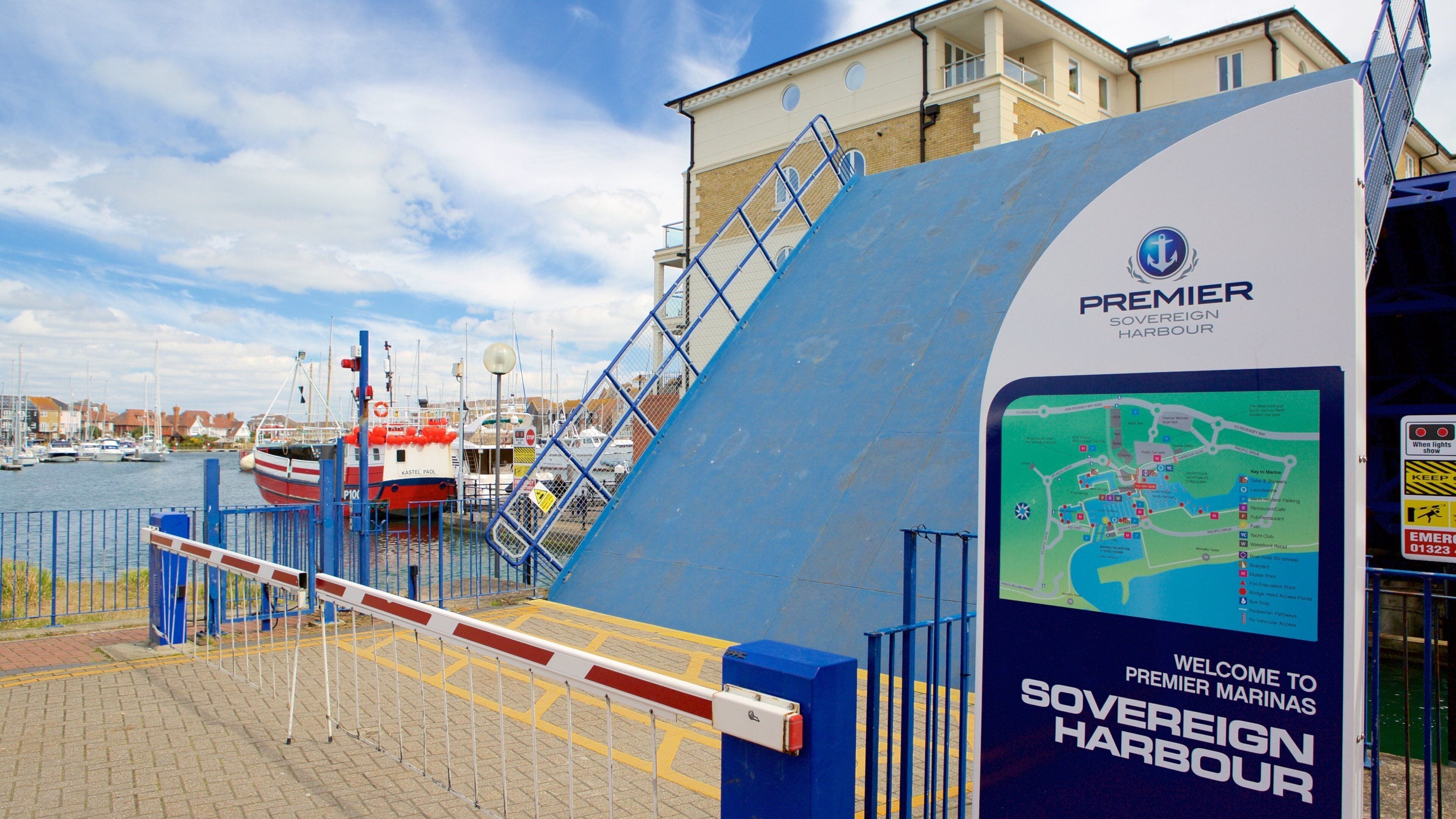A harbor entrance with a blue barrier gate, a sign for Premier Sovereign Harbour, and boats docked in the background.