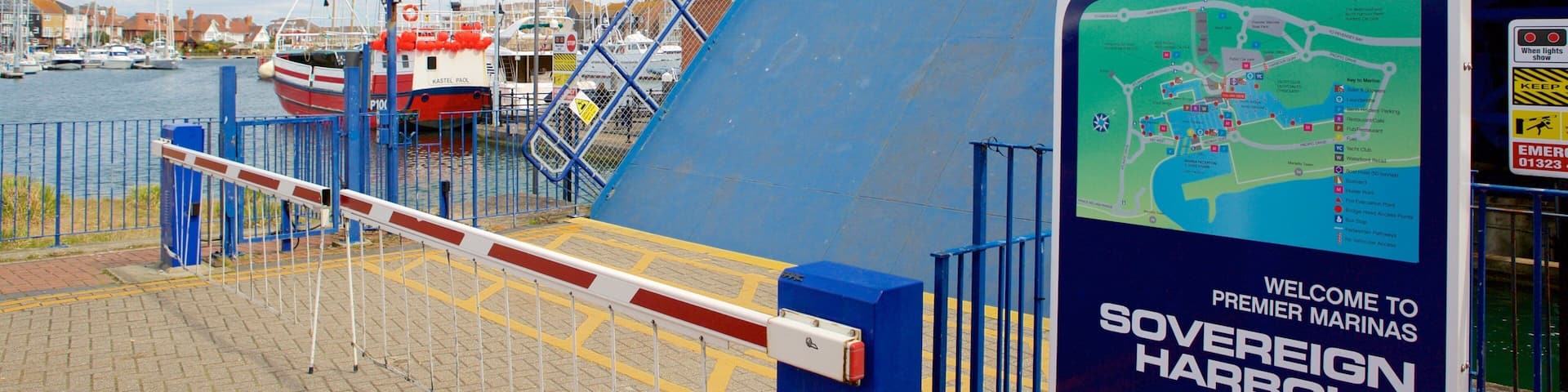 A harbor entrance with a blue barrier gate, a sign for Premier Sovereign Harbour, and boats docked in the background.