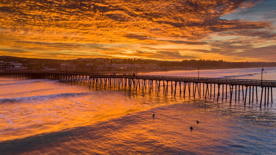 A sunset over a beach with a pier extending into the water.