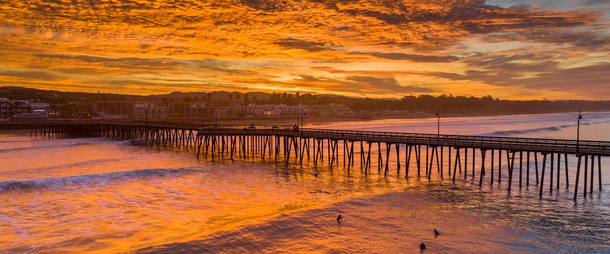 A sunset over a beach with a pier extending into the water.