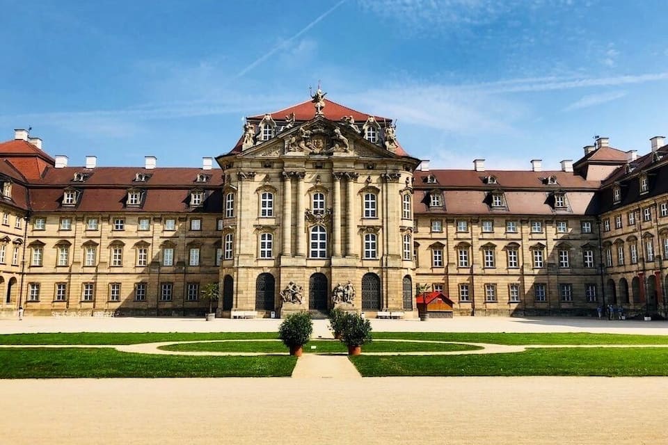 Un imposant bâtiment historique à l’architecture symétrique, doté d’une cour centrale et de statues.