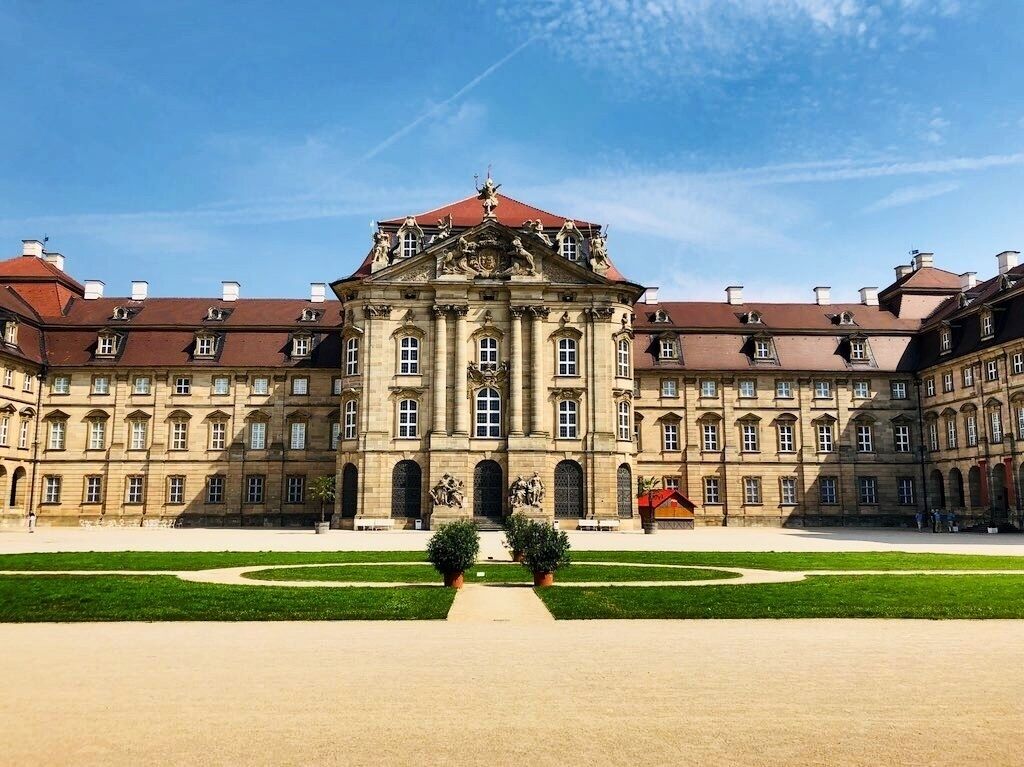 A grand historical building with symmetrical architecture, a central courtyard, and statues.