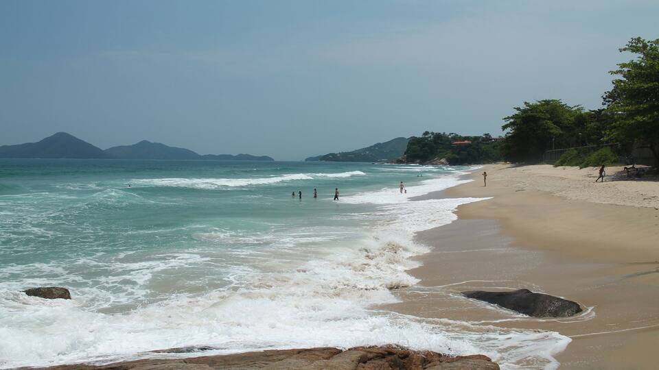 A beach with waves, people, and distant mountains.