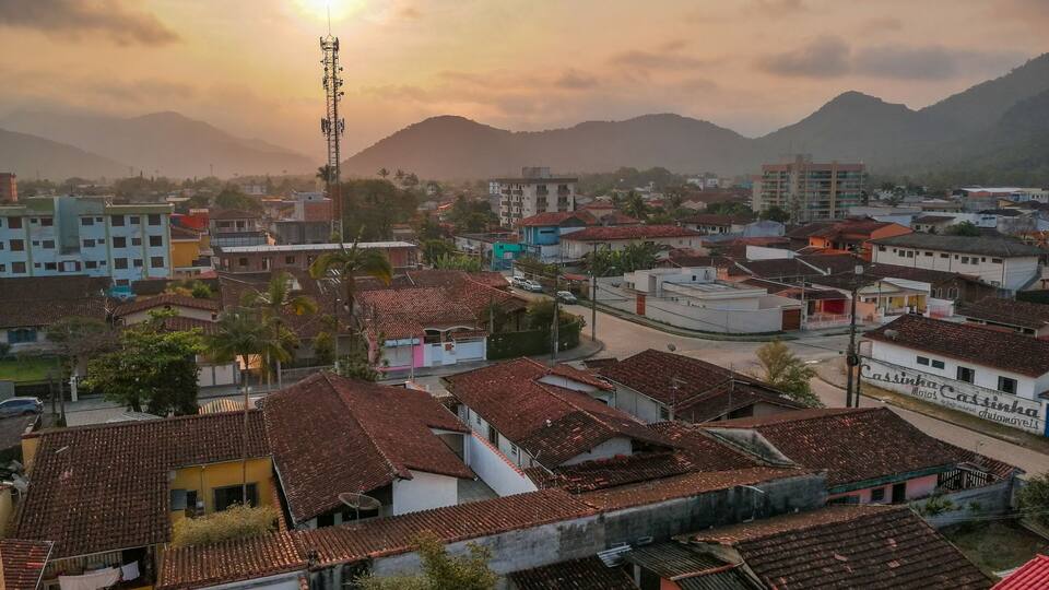 A town with red-tiled roofs, a prominent communication tower, and mountains in the background.