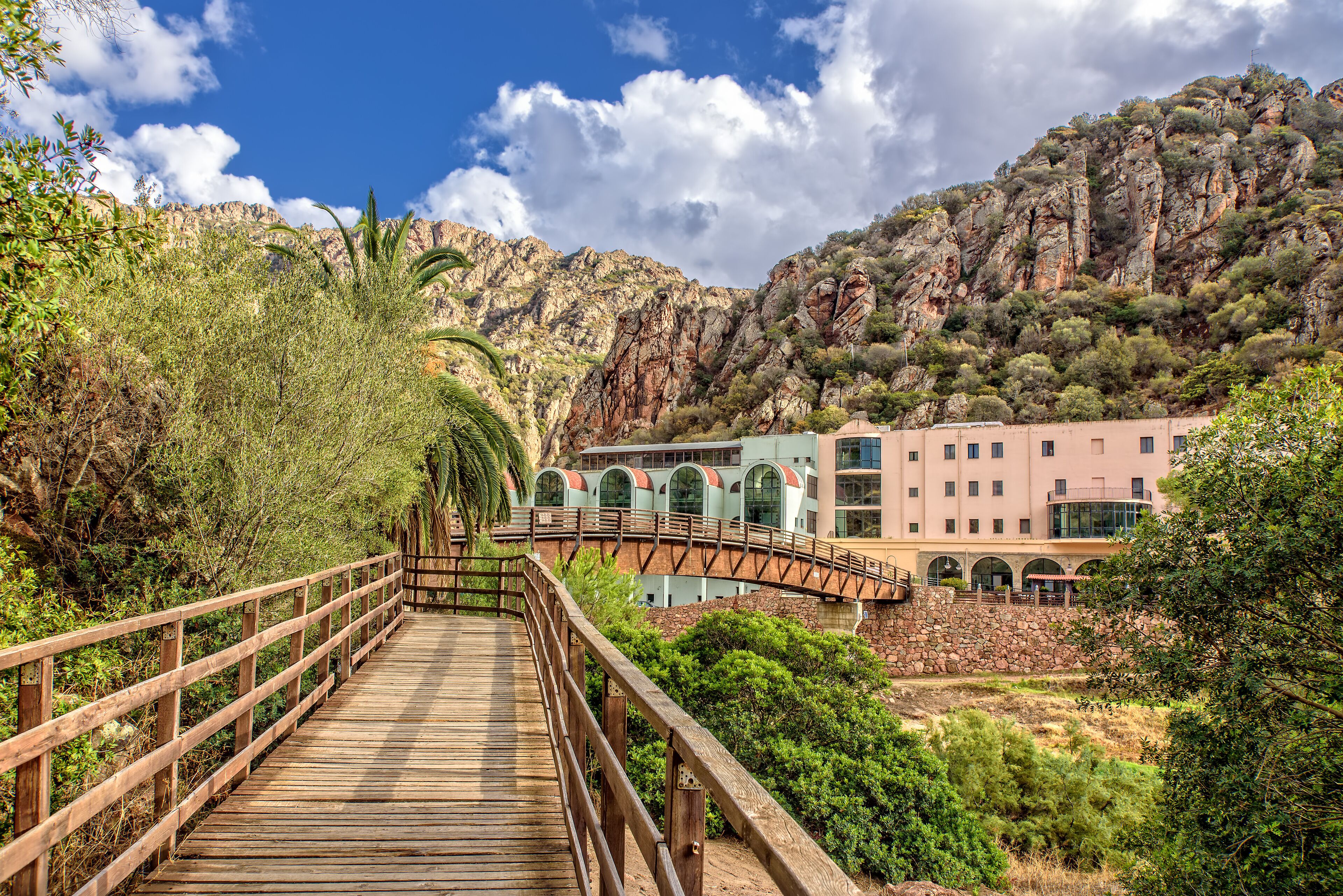 A wooden bridge leading to a building with arched windows and a stone wall.