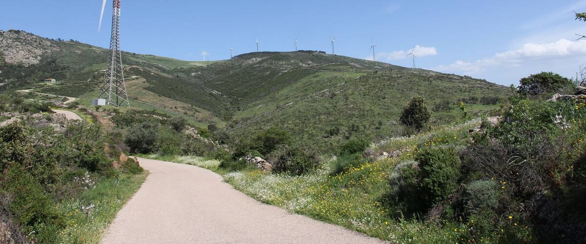 A winding road through a hilly landscape with wind turbines and a transmission tower.