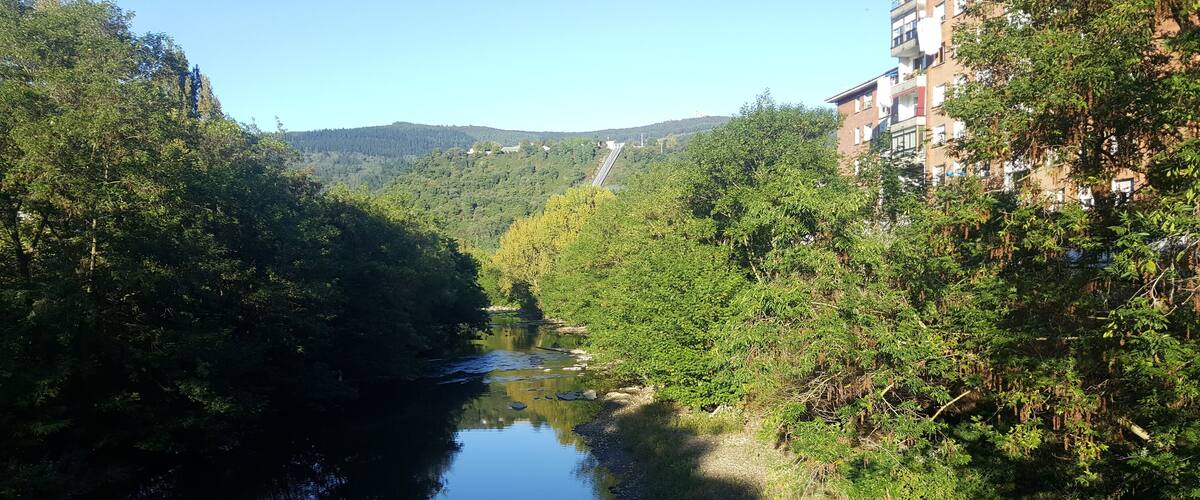A river flanked by dense greenery and a hillside with buildings.