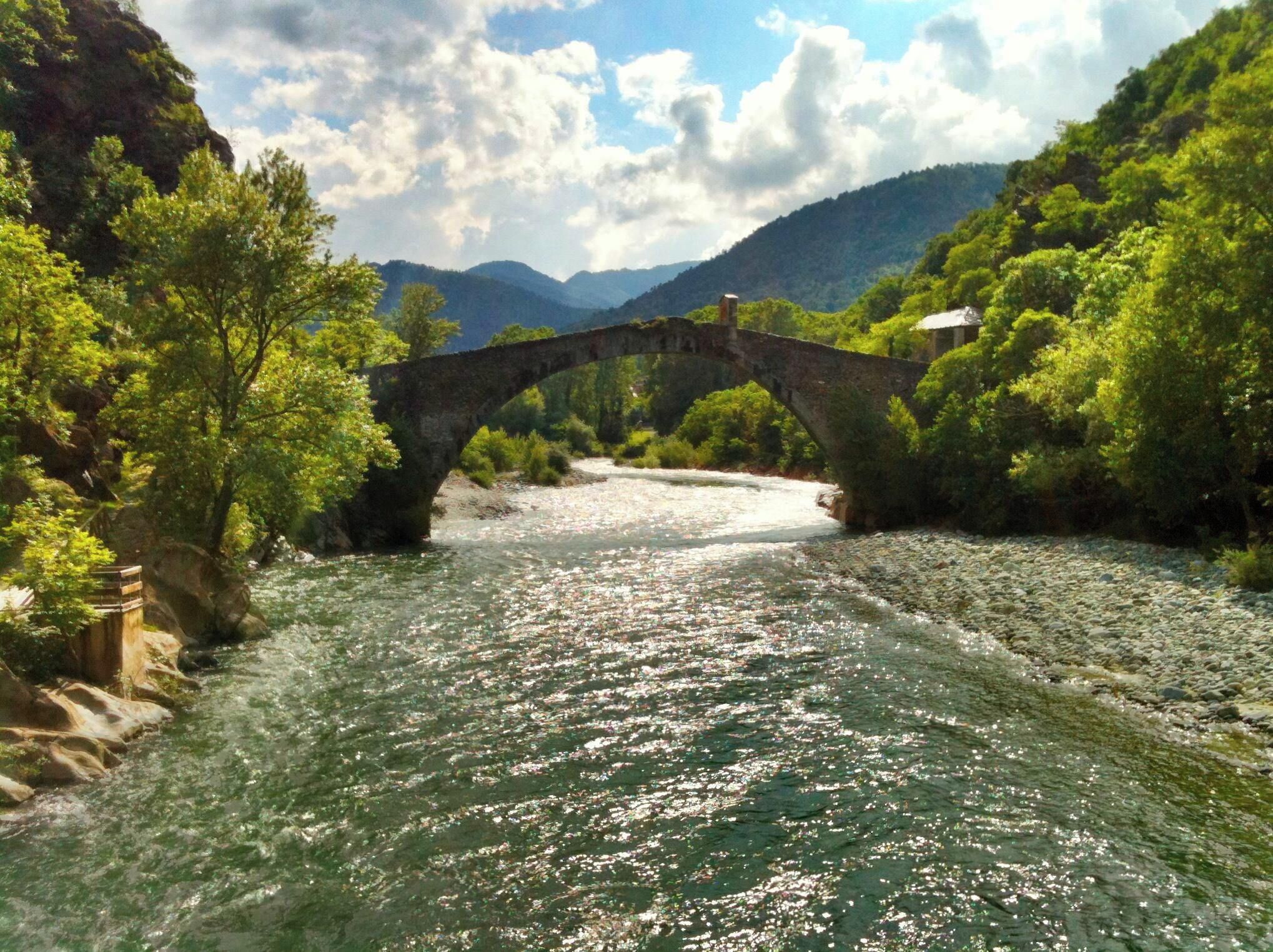 A stone bridge over a river surrounded by lush greenery and mountains.
