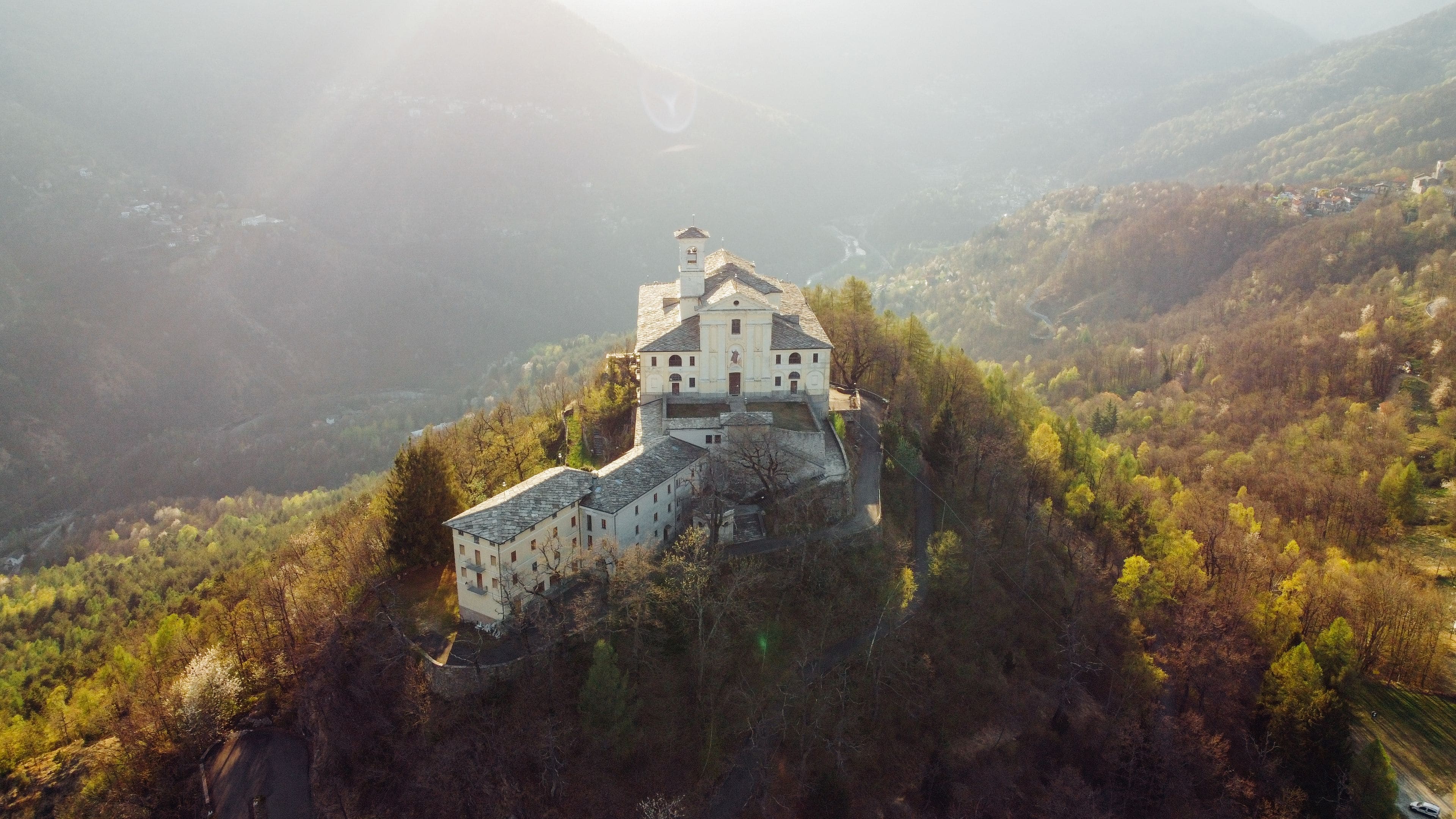 A white church with a bell tower on a hill surrounded by autumn foliage.