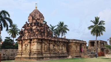 A detailed stone temple with intricate carvings and a large dome, surrounded by palm trees.