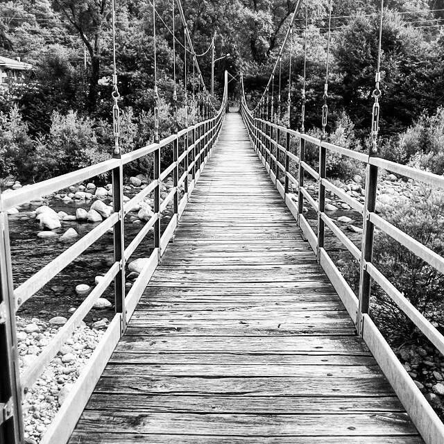 A wooden suspension bridge over a rocky stream surrounded by trees.