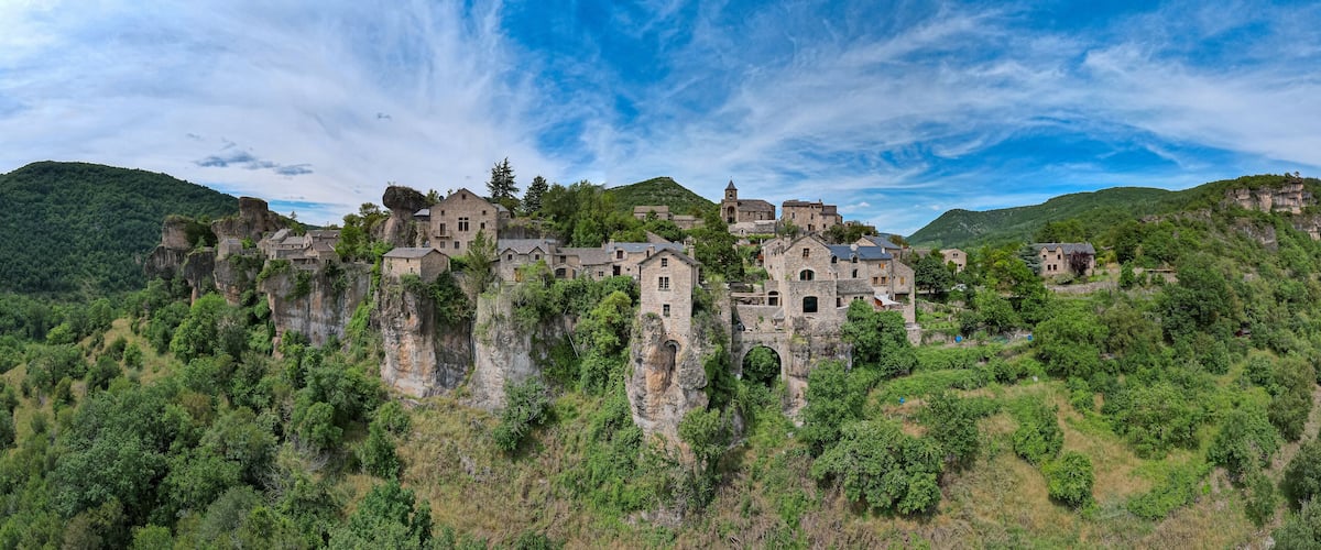 A historic stone castle perched on a cliff surrounded by lush greenery.