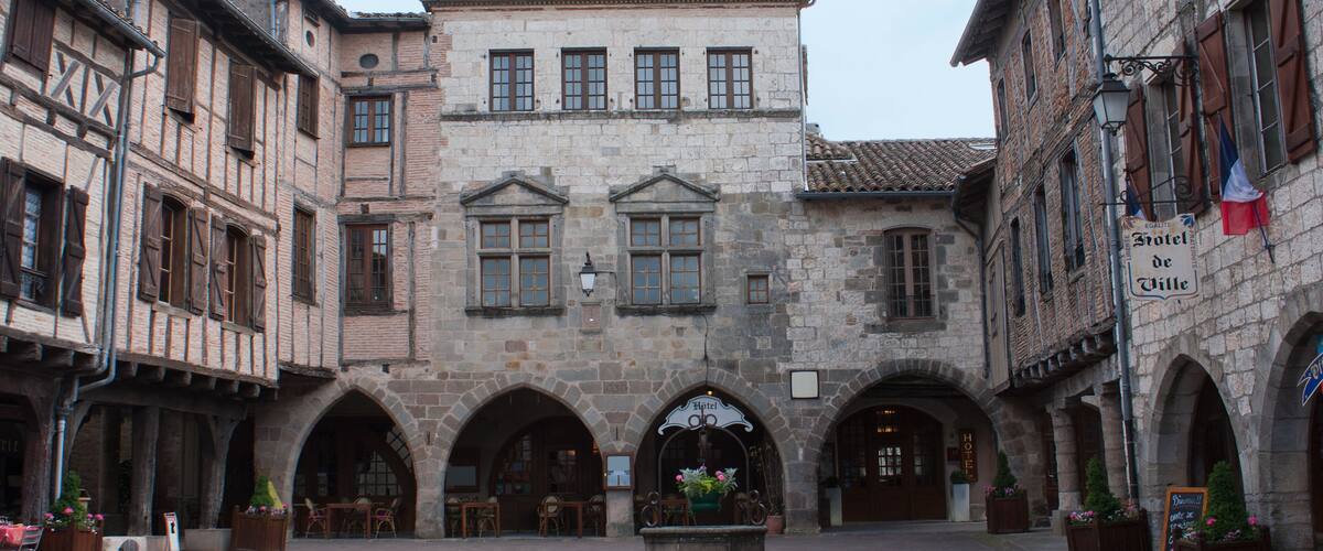 A historic square with a central fountain, surrounded by traditional half-timbered buildings and stone facades.