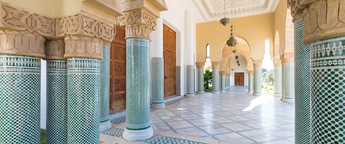 A grand hall with ornate columns and patterned floor tiles.